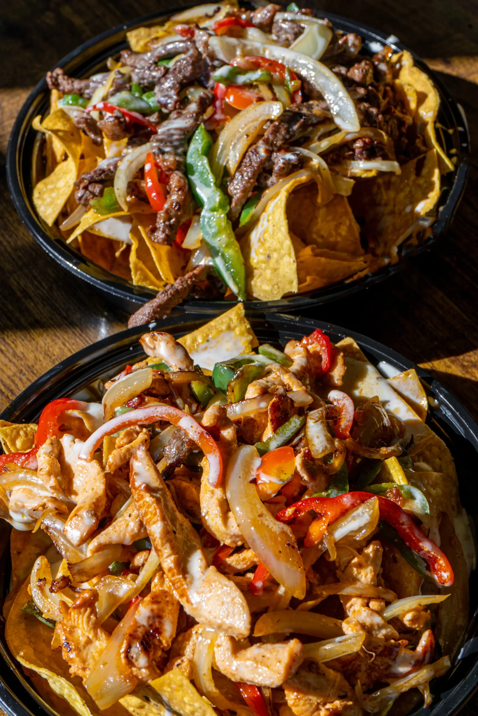 Two trays of fajita style nachos, one steak and one chicken, on a wooden table