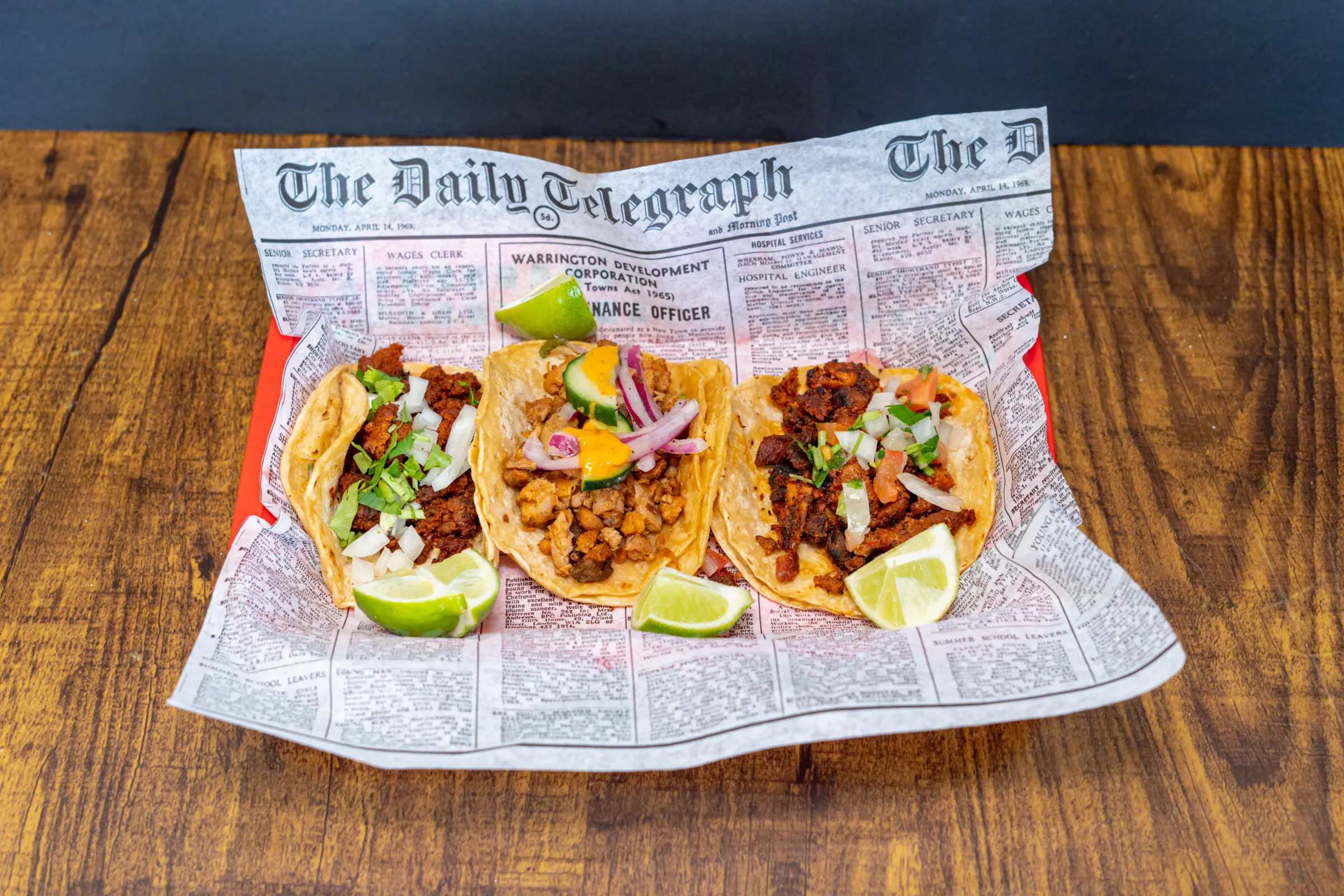 Three street tacos on newspaper paper with lime wedges
